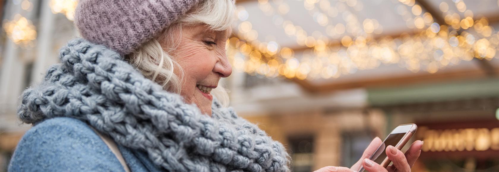 starsza pani w cieplej czapce na dworze, z komórką w reku