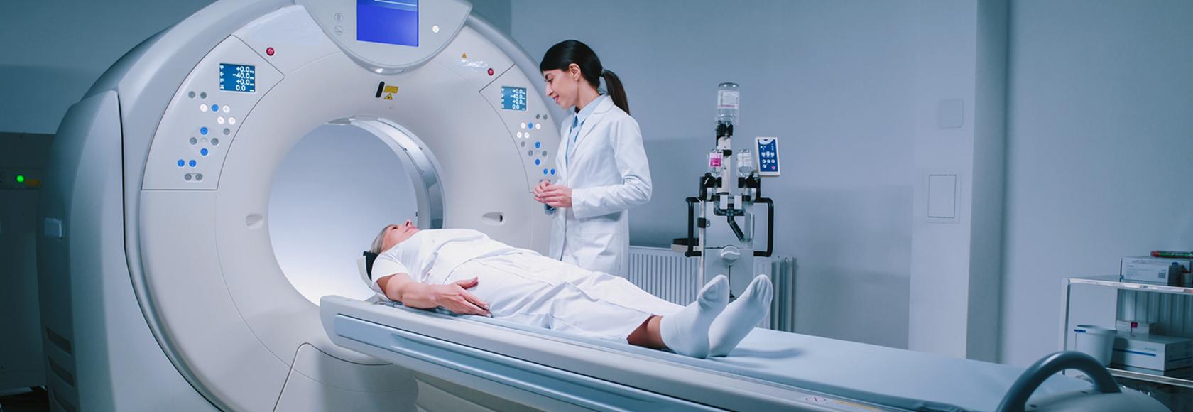 osoba leży na łóżku tomografu, obok stoi pielęgniarka