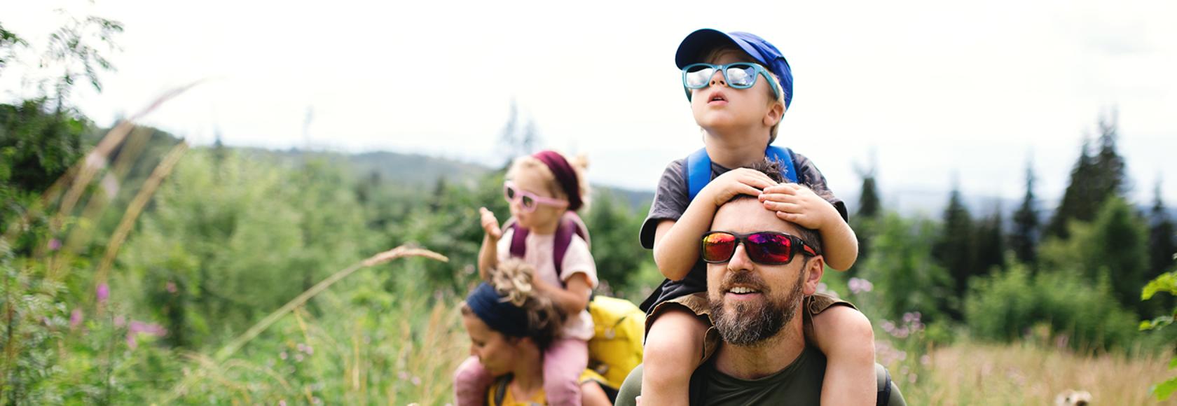 łąka z wysoką trawą, rodzice niosą dzieci na barana
