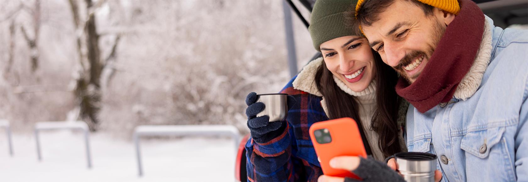 Usmiechnieta para patrzy na telefon, w tle zimowy krajobraz