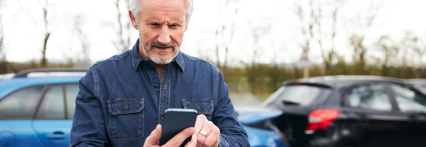 w tle zderzenie 2 aut mężczyzna z siwą bródką patrzy na telefon