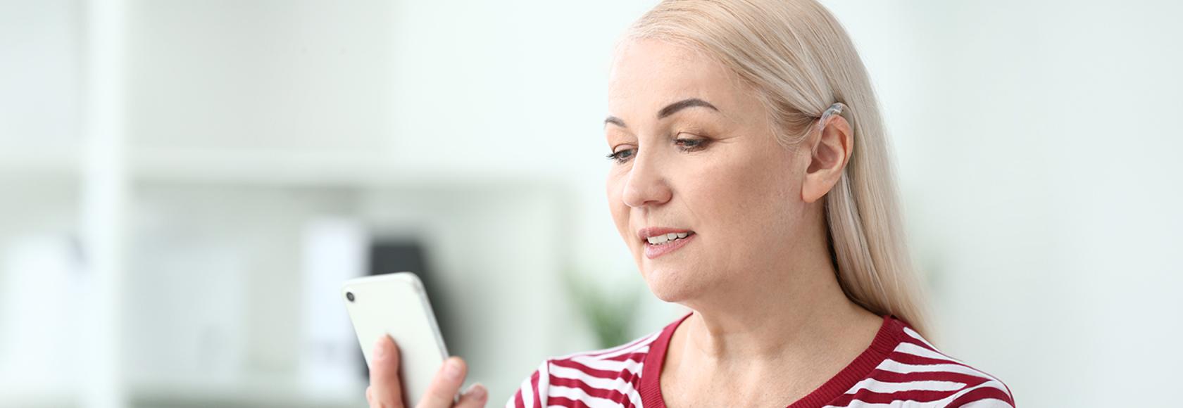 Blondynka z aparatem słuchowym patrzy na telefon 