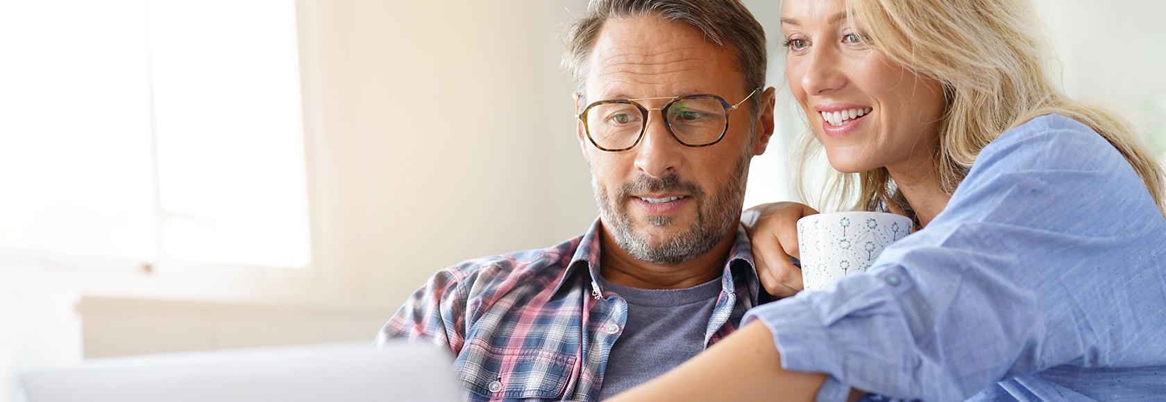 Kobieta z kubkiem kawy pokazuje coś na ekranie kompa mężczyźnie