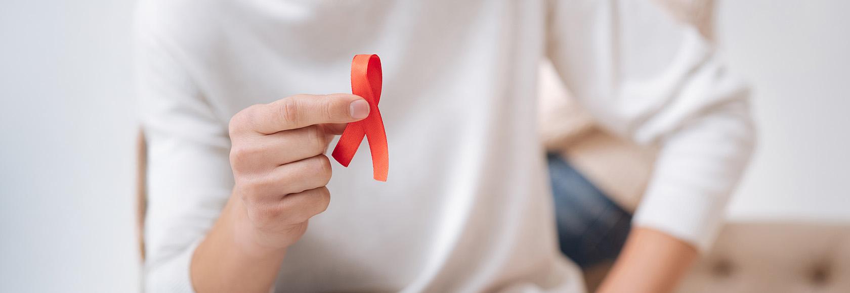 ręka trzymająca czerwoną wstążkę symbol AIDS