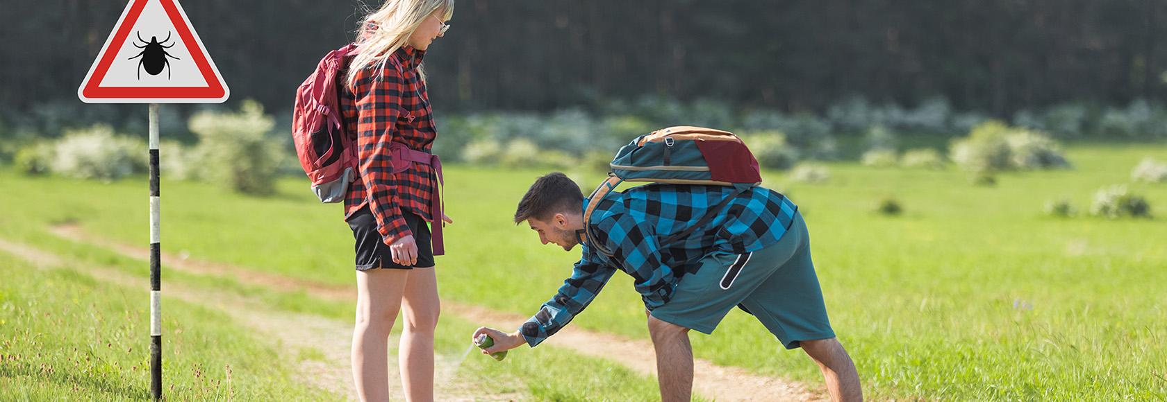 mężczyzna na lesniej drodze psika nogi kobiety aerozolem przeciw kleszczom
