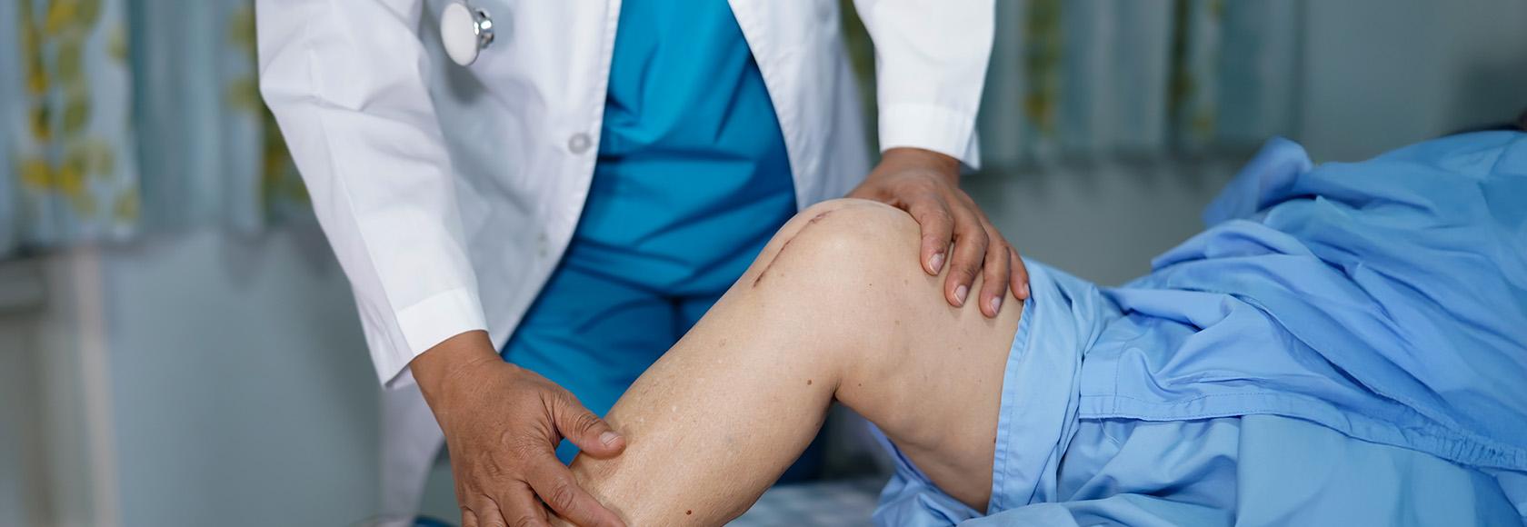 lekarz ogląda kolano pacjenta z blizną
