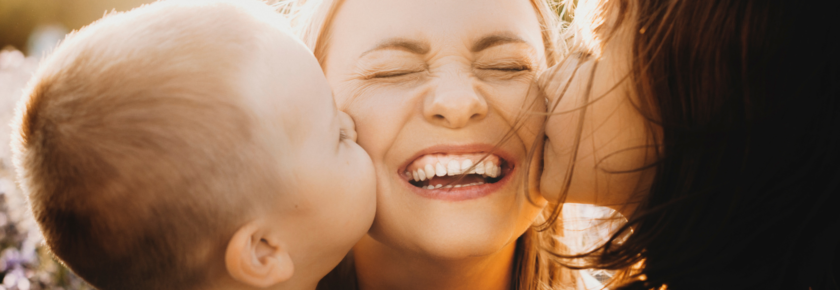 Dwoje dzieci całuje w policzki uśmiechniętą mamę