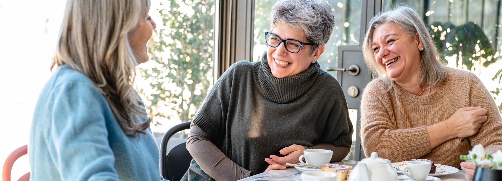 trzy kobiety w średnim wieku przy wspólnym stole, jedna patrzy na komórkę