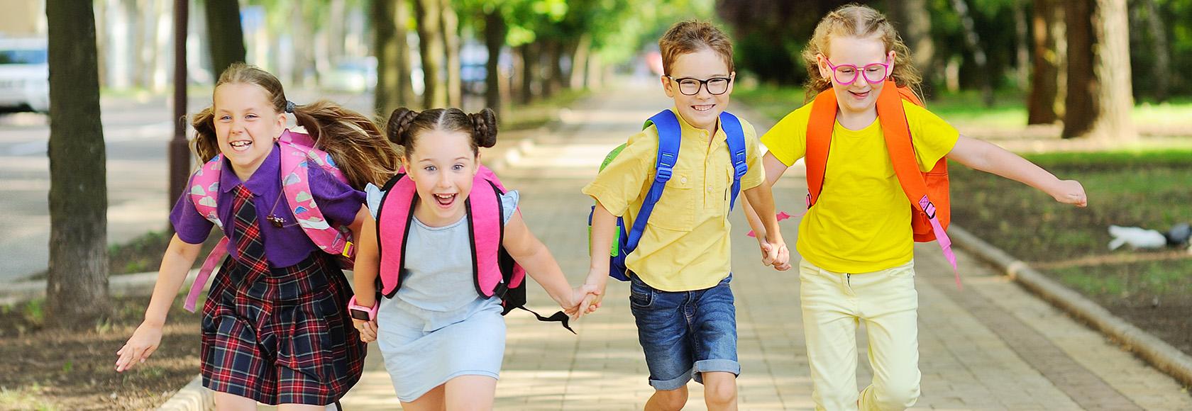 Czwórka dzieci ok. 10 lat z tornistrami, biegnie razem 