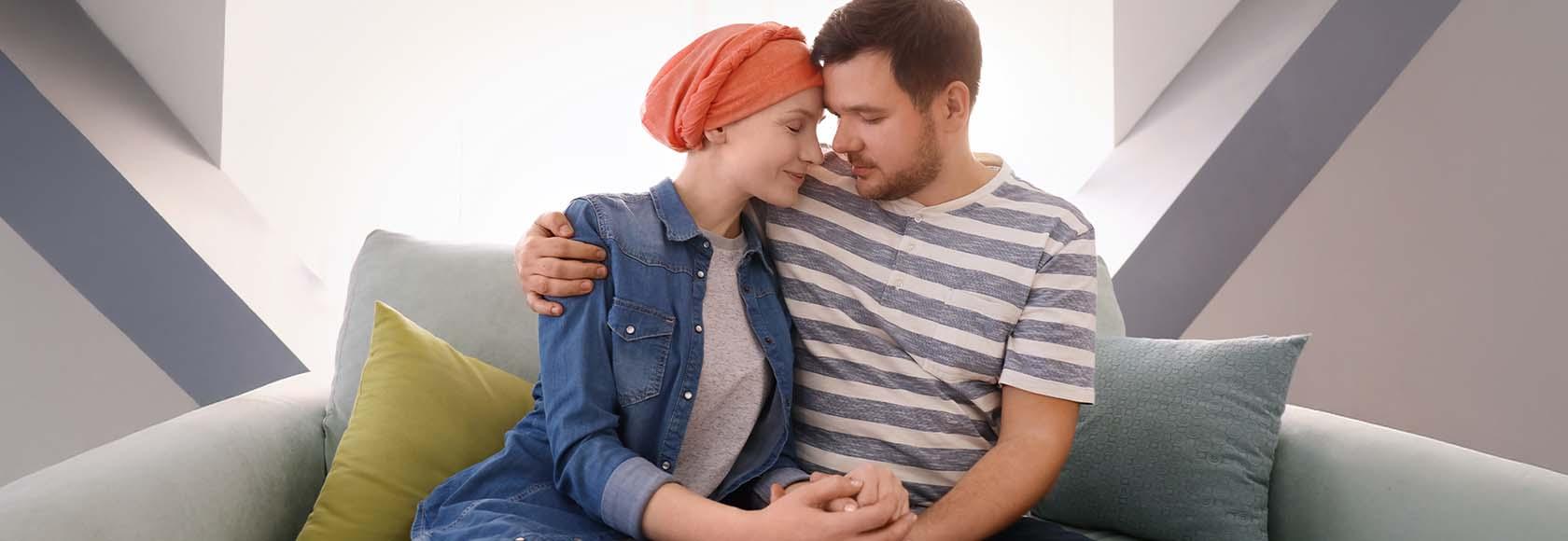 Młody mężczyzna i kobieta z chustką na głowie siedzą przytuleni na kanapie