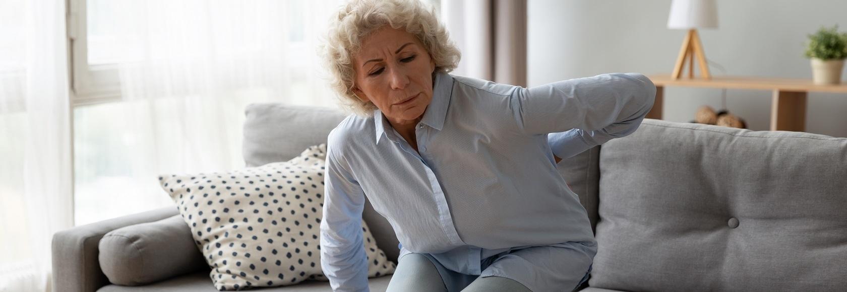 starsza pani z trudem siada na kanapie