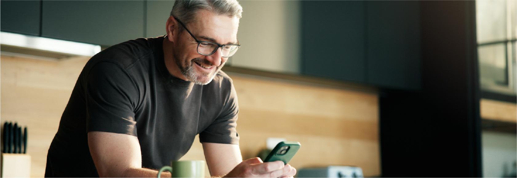 Pan z komórką w ręku, oparty łokciami o stół w kuchni