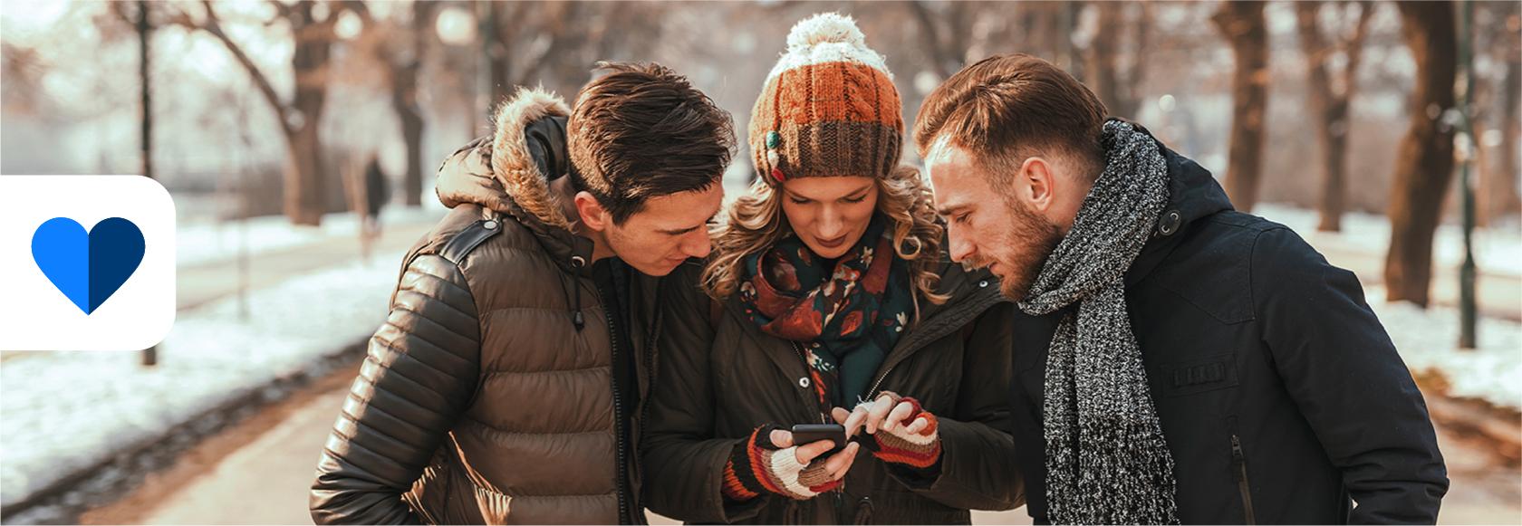 trzy osoby patrza w komorke trzymaną przez osobe w śrdoku