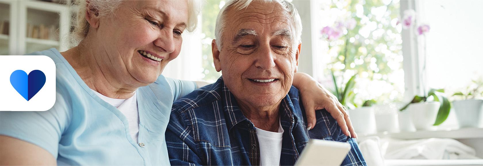 Starsza para na kanapie, żona pokazuje coś męzowi na komórce