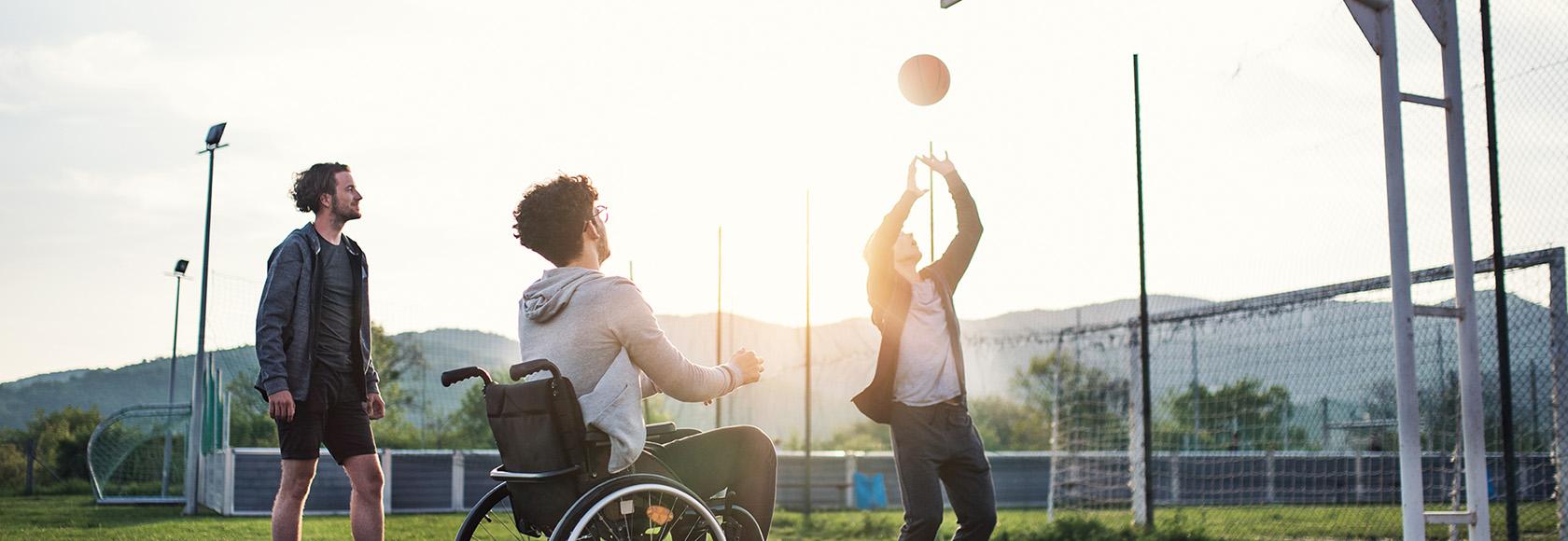 młodzi mężczyźni grają w koszykówkę, jeden jest na wózku