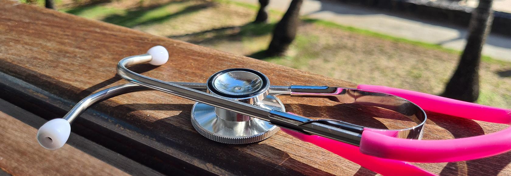 Różowy stetoskop leży na ławce w słońcu, w tle palmy i parasole na plaży