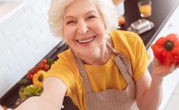 Uśmiechnięta, siwowłosa pani trzyma w ręku paprykę