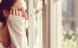Kobieta obejmuje rękami policzki i patrzy za okno