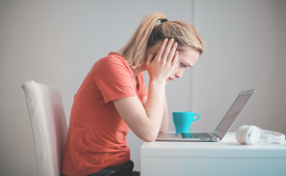 Dziewczyna ukazana bokiem, która siedzi przy biurku nad laptopem. Ma zatroskaną twarz. Łokcie opiera na blacie. Głowę ma opartą na dłoniach.