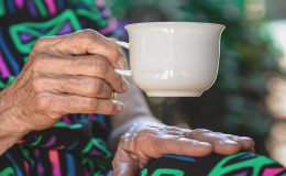 Wykadrowana starsza kobieta, która siedzi i w prawej ręce trzyma filiżankę. Widać ręce, filiżankę i fragment tułowia.