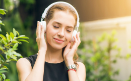 Uśmiechnięta dziewczyna z słuchawkami na uszach, na tle zieleni.