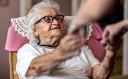 Starsza pani, której ktoś pomaga usiąść na łóżku