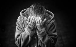 Starsza kobieta pochylona, z rękoma zasłaniącymi twarz.