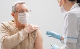 50latek w maseczce odsłania ramię do szczepienia