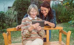 Dziewczyna pomaga zalogować się babci siedzącej na ławce w wiejskim ogródku