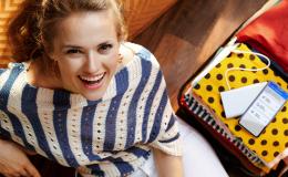 radosna kobieta, a na ubraniach w walizce leży komórka z UCC na ekranie