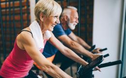 Starsza para ćwiczy na rowerkach stacjonarnych 