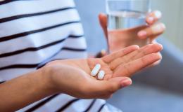 Wykadrowane ręce siedzącej osoby. W prawej ręce 2 tabletki, a w lewej szklanka z wodą