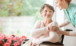 Uśmiechnięta starsza pani na wózku w towarzystwie młodej opiekunki