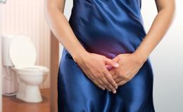 Wykadrowana kobieta z rękoma na układzie moczowym. Z lewej strony w tle toaleta.