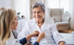 Młoda osoba pomaga się ubrać osobie starszej. Zapina guziki w jej koszuli zuli 