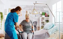 W domu pielęgniarka pomaga wstać starszej pani z łóżka