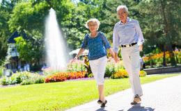 Para seniorów spacaruje po parku, w tle fontanna 