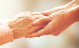 Zbliżenie na dłonie starszej osoby trzymane przez dłonie osoby młodszej