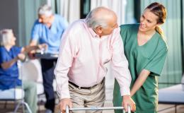 Starszy pan oparty o chodzik w asyscie pielęgniarki