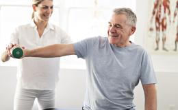 Starszy pan podnosi cieżarek z asystą fizjoterapeutki