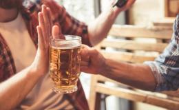 Mężczyzna podaje kufel z piwem koledze, ten odmawia dłonią blokując kufel.