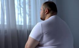 Otyły smutny mężczyzna siedzi na łóżku i patrzy w okno. 