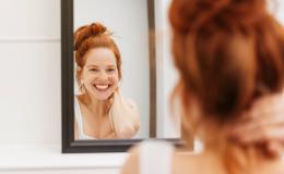 Uśmiechnięta kobieta stoi w łazience i przegląda się w lustrze.