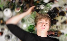 Nastolatek leży na podłodze, a dookoła niego stoją puste butelki po alkoholu.