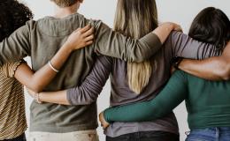 Cztery osoby stoją tyłem i obejmują się ramionami. 