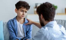 Trudna rozmowa ojca z synem. Chłopiec jest zasmucony, ojciec go wspiera, trzymając rękę na ramieniu.