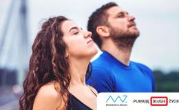 Młodzi kobieta i mężczyzna stoją z głowami skierowanymi ku niebu i oddychają pełną piersią świeżym powietrzem.