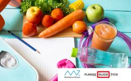 Leżące na deskach warzywa i owoce, waga, ciężarki, skakanka, szklanka z sokiem, kartka papieru