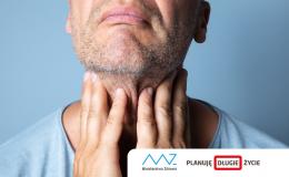 Mężczyzna dotyka palcami szyi. Na twarzy na grymas bólu. 