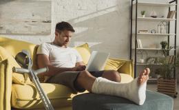 Mężczyzna z nogą w gipsie z komputerem na kolanach